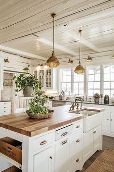 a kitchen with white cabinets and wooden counter tops, hanging lights over the sink and potted plant