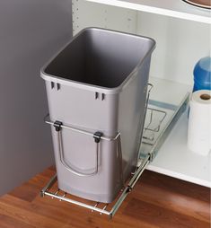 a metal trash can sitting on top of a wooden floor next to a white shelf