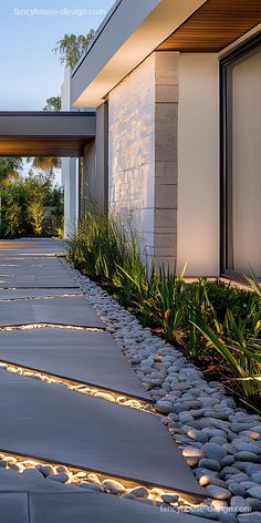 the walkway is lined with stones and plants next to a modern house at night time