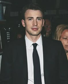 a man in a suit and tie is looking at the camera while people look on