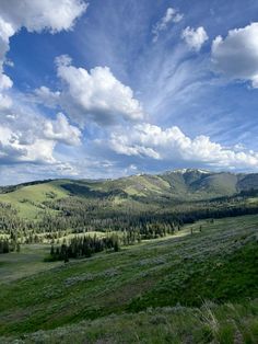 the mountains are covered in green grass and blue skies with white fluffy clouds above them