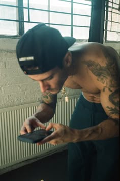 a tattooed man holding a cell phone in his right hand and looking at the screen