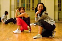 two young women sitting on the floor in a dance studio, one smiling at the camera