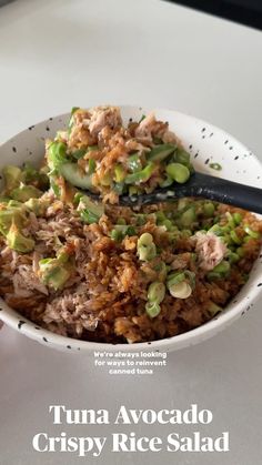 a white bowl filled with tuna and rice salad on top of a table next to a fork
