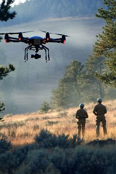 two men standing in the grass with a remote controlled flying device above their heads,