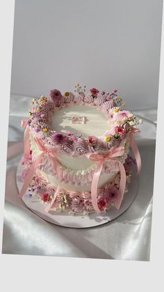 a three layer cake decorated with pink flowers and ribbons on a white tableclothed surface