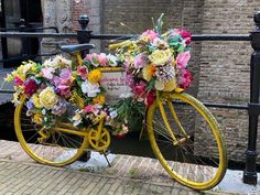 a yellow bicycle with flowers on the front and back wheel is parked in front of a brick building