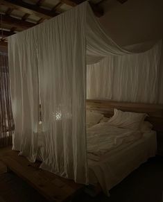 an unmade bed with white drapes hanging from it's sides in a dark room