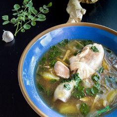 a blue bowl filled with soup next to some fresh herbs and garlic on a black table