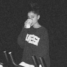 a young woman drinking from a cup while standing next to a stair case in the dark