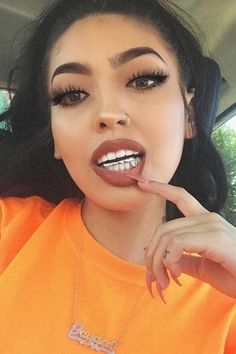 a woman in an orange shirt is holding her finger up to her lips and looking at the camera