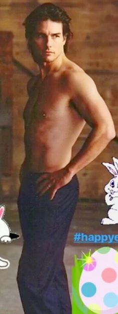 a man with no shirt standing in front of a wooden wall and wearing blue pants