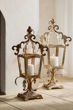 two metal candle holders sitting on top of a floor next to each other with candles in them