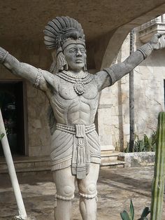 a statue of a man with his arms outstretched in front of a cactus and building