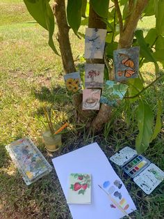 some cards are laying on the ground next to a tree and paintbrushes with watercolors