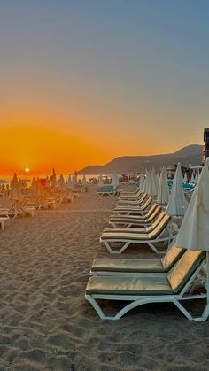 the sun is setting at the beach with lounge chairs and umbrellas lined up on the sand