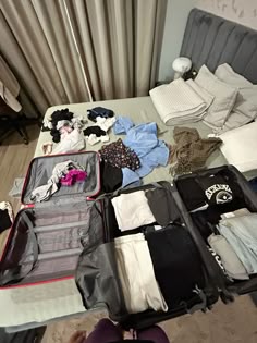 an open suitcase sitting on top of a bed next to clothes and other clothing items