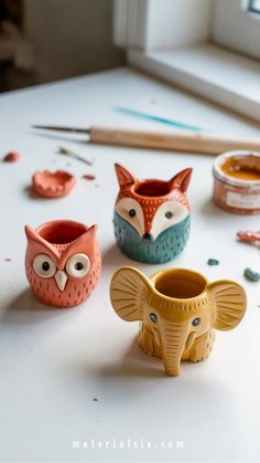 Colorful ceramic pots shaped like an owl, fox, and elephant, surrounded by crafting tools and materials.