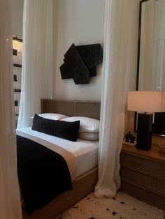 a bed with black and white pillows in a bedroom next to a mirror on the wall