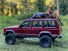 a woman sitting on top of a red jeep