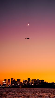 an airplane is flying over the city at sunset or dawn with a crescent moon in the sky