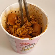 a cup filled with noodles and chopsticks on top of a white countertop