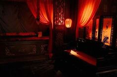a dark room with red curtains and a bench in the center, lit by lanterns