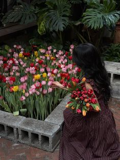 a woman in a long dress is picking flowers out of a planter on the sidewalk