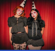 two women dressed up as clowns posing for the camera with red curtains behind them