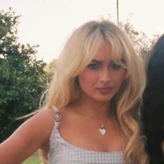 a woman with blonde hair standing next to a black dog and wearing a white top