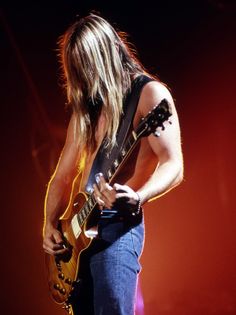a man with long hair playing an electric guitar