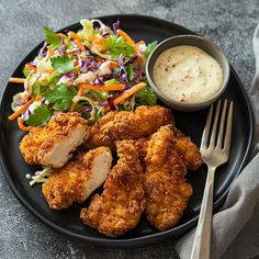 a black plate topped with fried chicken and salad next to a bowl of ranch dressing