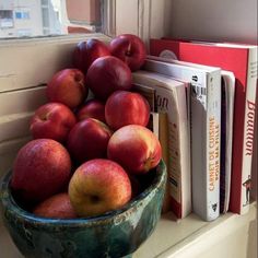 a bowl filled with apples sitting on top of a window sill next to books