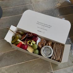 a box filled with assorted snacks on top of a tiled floor next to a bottle of wine