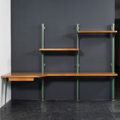 three wooden shelves with green metal brackets on them against a gray wall in an empty room