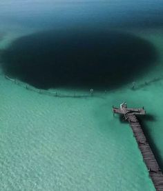 an aerial view of the ocean with a dock in the water and people standing on it