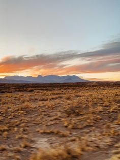 the sun is setting in the desert with mountains in the backgrouds and grass on the ground