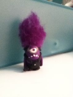 a small toy with purple hair sitting on top of a white table next to a mirror