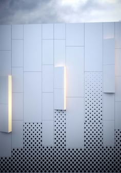 an abstract white wall with perfored panels and lights on the side, in front of a cloudy sky