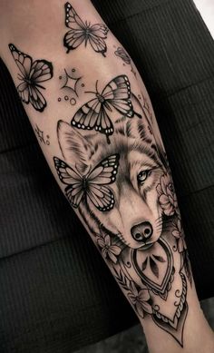 a black and white tattoo with a wolf on it's leg, surrounded by butterflies