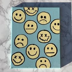 a blue box with yellow smiley faces painted on the front and sides, sitting on a marble surface