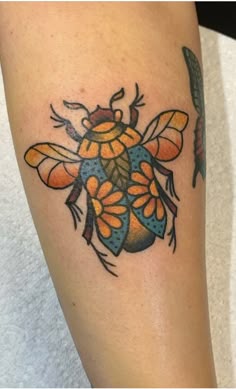 a colorful tattoo on the leg of a ladybug with leaves and flowers around it