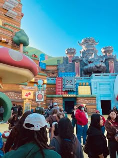 many people are standing in front of an amusement park ride at disneyland world, with the theme park's mushroom house behind them