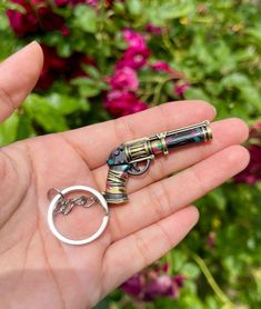 a hand holding a small metal object in it's right hand, with flowers in the background