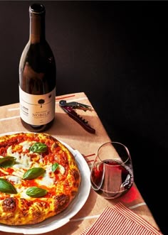 a pizza sitting on top of a white plate next to a wine bottle and glass