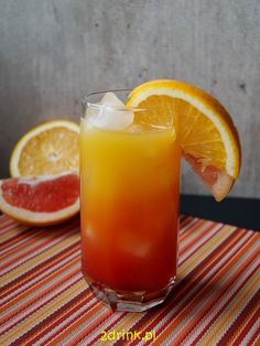 an orange drink with ice and garnish on a striped table cloth next to two grapefruits