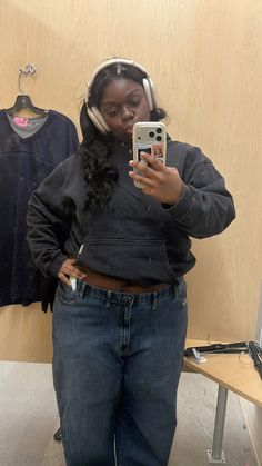 a woman is wearing headphones and looking at her cell phone while standing in front of a wooden wall