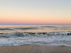 the waves are coming in to the shore at sunset on the beach with pink and blue sky