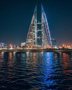 a very tall building sitting in the middle of a body of water with lights on it's sides