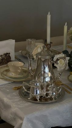 a silver tea pot sitting on top of a table next to a white flower arrangement
